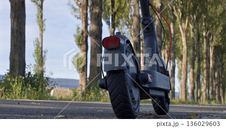 Electric scooter parked on a quiet path lined with trees near open fields during daylight hours Electric scooter parked on a quiet path lined with trees near open fields during daylight hours 136029603