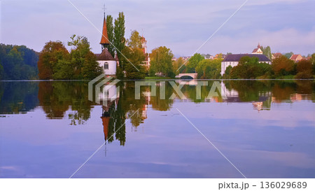 Scenic view of a church and houses by the water reflecting at sunrise in a quiet town Scenic view of a church and houses by the water reflecting at sunrise in a quiet town 136029689