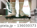 Close-up image of a person's feet while standing on a weighing scale, with a virtual screen displaying various body measurements. 136030373
