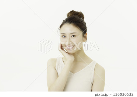 白背景のタンクトップを着てアップヘアの頬に手を当てて微笑む若い日本人女性 136030532