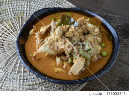 A Panang curry with chicken, long beans, turkey berries, and kaffir lime leaves is served in a ceramic bowl. 136032243