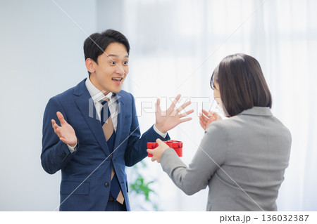 社内で男性にプレゼントを渡す女性 社内で男性にプレゼントを渡す女性 136032387