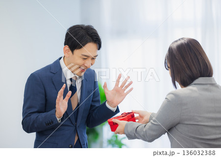 社内で男性にプレゼントを渡す女性 社内で男性にプレゼントを渡す女性 136032388