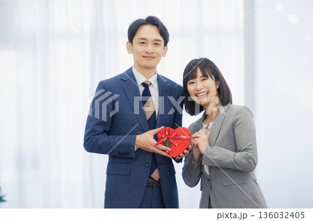 社内で男性にプレゼントを渡す女性 社内で男性にプレゼントを渡す女性 136032405