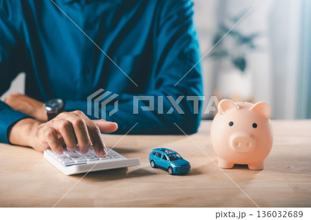 Man calculates auto car loan payments, managing piggy bank money, saving for insurance, bank debt, tax, planning financial safety, securing future investment 136032689