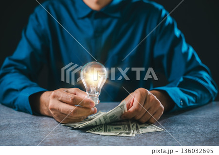 Glowing light bulb idea for business innovation and growth concept, businessman counting currency bank notes on table shows financial success and global marketing management 136032695