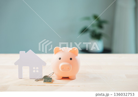 Pink piggy bank sitting beside white house model and metal keys on wooden surface signifies real estate investment, money saving for property ownership, and home insurance planning 136032753
