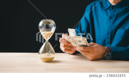 Money management, time, glass hourglass on table, person holding dollar banknotes, concept for business investment, global finance, saving and banking 136032855