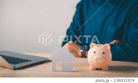 Real estate investment involves money saving with piggy bank for house property, insurance for home, man using laptop to save for purchase, planning financial security and mortgage Real estate investment involves money saving with piggy bank for house property, insurance for home, man using laptop to save for purchase, planning financial security and mortgage 136032874