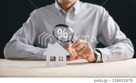 Real estate appraisal inspector uses magnifying glass to search for home property valuation, revealing percentage symbol over house model for financial inspection details 136032879