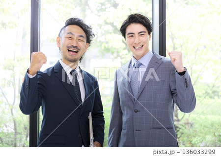 新緑の窓が綺麗なオフィスでビジネスマンのガッツポーズのカメラ目線大笑い　達成や成功のイメージ	 136033299