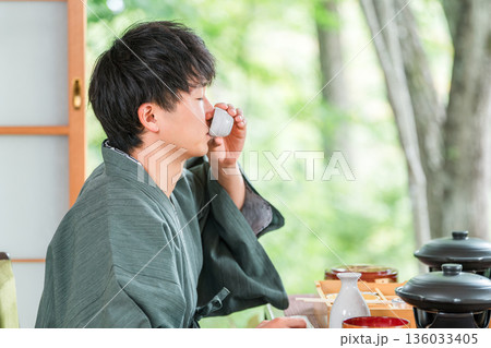 旅館で会席料理で日本酒を楽しむ若いアジア人男性（部屋食・懐石料理・御膳・贅沢） 136033405