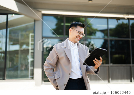 Happy businessman raising fist and cheering with smartphone in hand, celebrating success and victory with excitement and joy outdoors. Happy businessman raising fist and cheering with smartphone in hand, celebrating success and victory with excitement and joy outdoors. 136033440