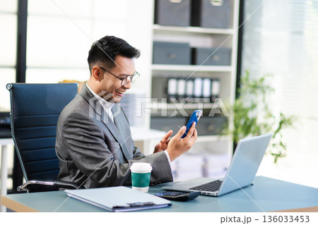 Asian man using laptop and tablet while sitting at her working place. Concentrated at work. 136033453