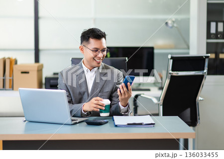Asian man using laptop and tablet while sitting at her working place. Concentrated at work. Asian man using laptop and tablet while sitting at her working place. Concentrated at work. 136033455