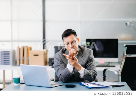Tired businessman suffering neck pain from office syndrome, feeling muscle strain and discomfort while working long hours at desk with laptop. 136033555