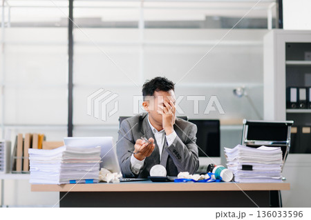 Exhausted businessman holding coffee cup at desk, feeling tired and overworked with paperwork and deadlines in modern office environment. 136033596