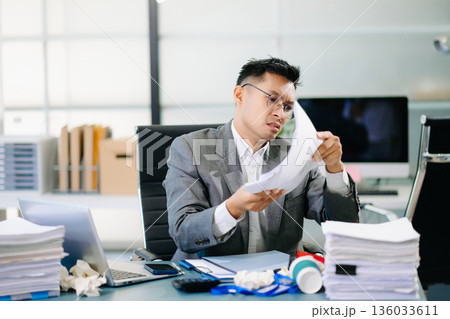 Focused office worker analyzing documents, reviewing business reports with stress and concentration in workplace setting. 136033611