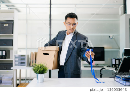 Depressed businessman packing box after job loss, feeling sad and stressed from layoff or resignation in modern office environment. Depressed businessman packing box after job loss, feeling sad and stressed from layoff or resignation in modern office environment. 136033648
