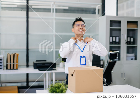 Asian office worker packing belongings into a cardboard box, representing resignation, job change, or a fresh career start in a modern workplace environment. Asian office worker packing belongings into a cardboard box, representing resignation, job change, or a fresh career start in a modern workplace environment. 136033657