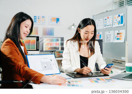Two professional women designers discussing UX UI and color palette in a creative modern office. Ideal for teamwork, innovation Two professional women designers discussing UX UI and color palette in a creative modern office. Ideal for teamwork, innovation 136034300