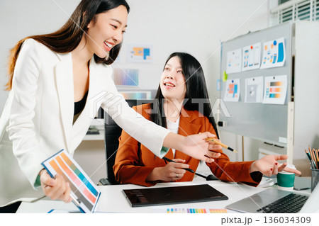 Two creative female designers discussing color palettes and UX UI project in a modern office. Perfect for teamwork, innovation, and digital design themes. 136034309