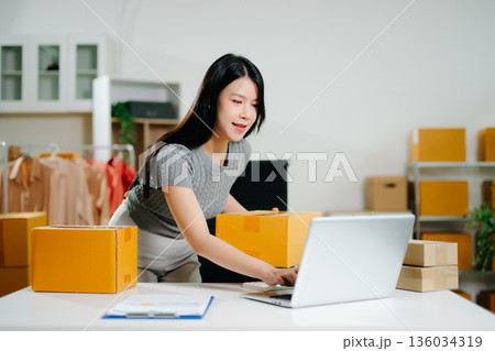 Startup small business SME, Entrepreneur owner woman using smartphone or tablet taking receive and checking online purchase shopping order to preparing pack product box. Startup small business SME, Entrepreneur owner woman using smartphone or tablet taking receive and checking online purchase shopping order to preparing pack product box. 136034319