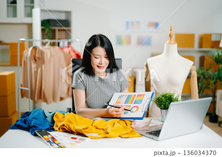 Asian fashion designer working in studio with mannequin, fabric and laptop. Creative fashion business, tailor planning clothing design Asian fashion designer working in studio with mannequin, fabric and laptop. Creative fashion business, tailor planning clothing design 136034370