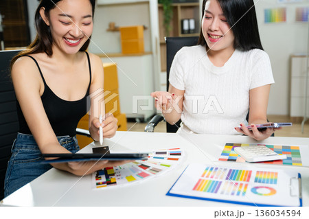 Fashion designers working together in a studio with color palettes, tablet, and sketches. Creative teamwork, modern workspace, textile planning Fashion designers working together in a studio with color palettes, tablet, and sketches. Creative teamwork, modern workspace, textile planning 136034594
