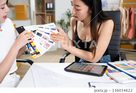 Fashion designers collaborating with color palettes, sketches, and digital tools in a studio. Creative design process, branding, textile planning 136034622