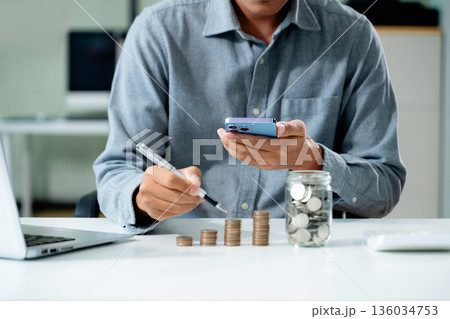 businessman holding coins putting in glass with using smartphone and calculator to calculate concept saving money 136034753