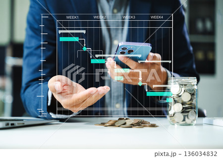 Project planning and finance concept with Gantt chart, coins, and smartphone in office. Businessman visualizes productivity Project planning and finance concept with Gantt chart, coins, and smartphone in office. Businessman visualizes productivity 136034832
