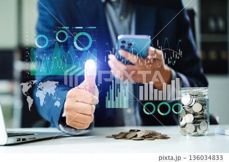 Businessman uses smartphone for virtual fintech analysis. Coins, charts, and futuristic UI symbolize financial success, investments 136034833