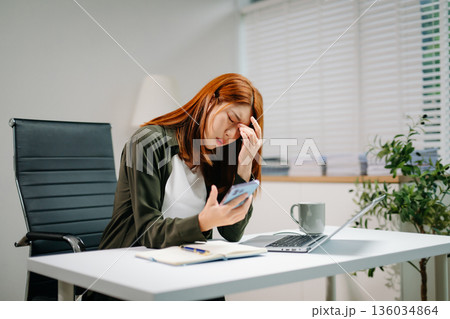 Young Asian woman in office showing signs of stress and burnout while working on laptop. Concept of overwork Young Asian woman in office showing signs of stress and burnout while working on laptop. Concept of overwork 136034864