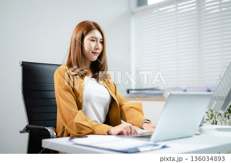 Confident Asian business people using laptops, tablets, and phones in modern office workspace, planning data strategy and success. Confident Asian business people using laptops, tablets, and phones in modern office workspace, planning data strategy and success. 136034893