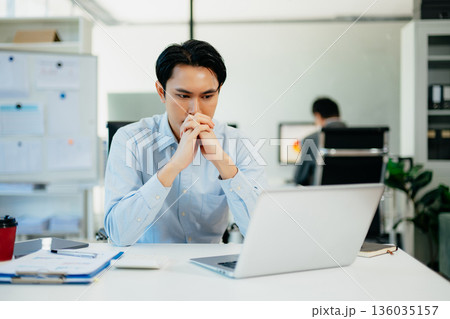 Asian businessman is stressed, bored, and overthinking from working on a tablet at the modern office. 136035157