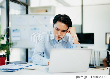 Asian man feeling migraine head strain.Overworked businessman financier while working on laptop and tablet at office. Asian man feeling migraine head strain.Overworked businessman financier while working on laptop and tablet at office. 136035158