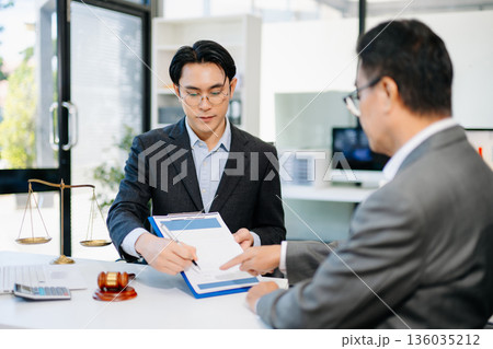 Lawyer advising client on contract signing in modern office, with gavel and scales of justice. Perfect for law, finance, consulting, or business concepts. 136035212