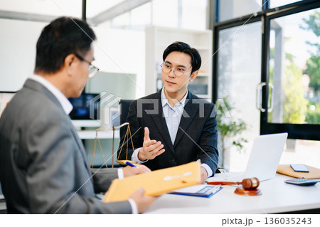 Lawyer consulting client in modern office, reviewing documents with gavel and scales on desk. Ideal for law, finance, consulting, or corporate themes. Lawyer consulting client in modern office, reviewing documents with gavel and scales on desk. Ideal for law, finance, consulting, or corporate themes. 136035243