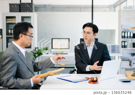 Lawyer consulting client in modern office, reviewing documents with gavel and scales on desk. Ideal for law, finance, consulting, or corporate themes. Lawyer consulting client in modern office, reviewing documents with gavel and scales on desk. Ideal for law, finance, consulting, or corporate themes. 136035246