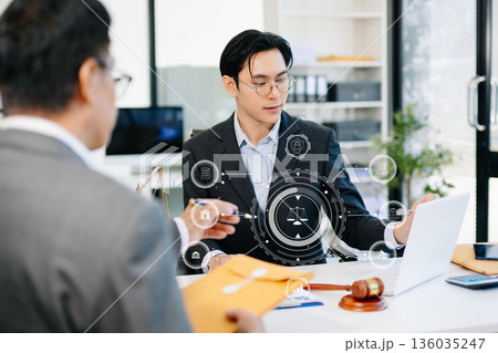 Lawyer consulting client in modern office, reviewing documents with gavel and scales on desk. Ideal for law, finance, consulting, or corporate themes. Lawyer consulting client in modern office, reviewing documents with gavel and scales on desk. Ideal for law, finance, consulting, or corporate themes. 136035247