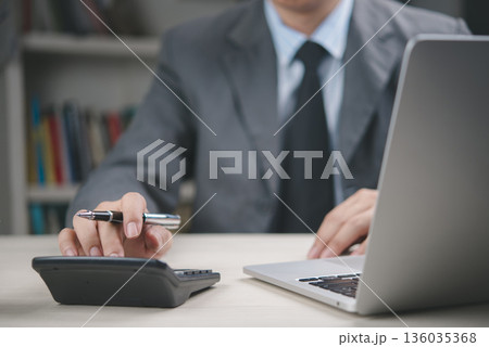 Businessman using calculator and laptop in office, working on financial report, accounting, business management, investment planning, tax calculation, corporate finance and data analysis. 136035368