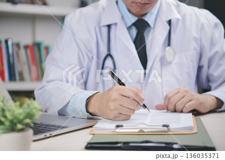 Doctor in white coat signing medical agreement on desk, confirming approval, patient data record, healthcare validation, legal documentation, official certification, hospital paperwork. Doctor in white coat signing medical agreement on desk, confirming approval, patient data record, healthcare validation, legal documentation, official certification, hospital paperwork. 136035371