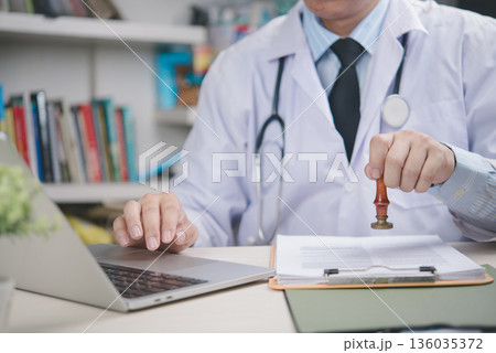 Doctor stamping medical document in office, confirming approval, healthcare certification, hospital paperwork validation, professional authority, legal record and patient management concept. Doctor stamping medical document in office, confirming approval, healthcare certification, hospital paperwork validation, professional authority, legal record and patient management concept. 136035372