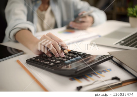 businesswoman using a calculator and analyzing business charts and graphs on desk. financial management, tax planning, and strategic budget analysis. businesswoman using a calculator and analyzing business charts and graphs on desk. financial management, tax planning, and strategic budget analysis. 136035474