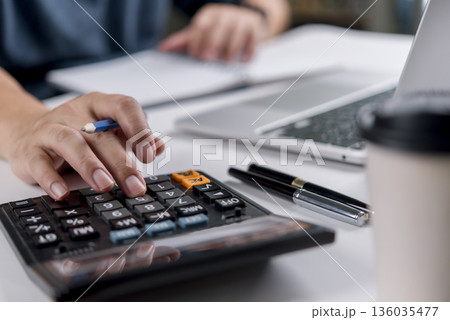accountant or financial advisor working on a desk with a calculator, notebook, and a laptop computer. concepts of budget management, tax preparation, and financial planning for businesses. accountant or financial advisor working on a desk with a calculator, notebook, and a laptop computer. concepts of budget management, tax preparation, and financial planning for businesses. 136035477