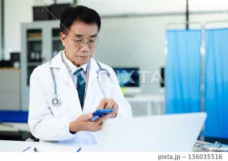 Asian doctor working on laptop and writing notes in modern clinic. Ideal for healthcare, diagnosis, medical research, and professional consultation themes. Asian doctor working on laptop and writing notes in modern clinic. Ideal for healthcare, diagnosis, medical research, and professional consultation themes. 136035516