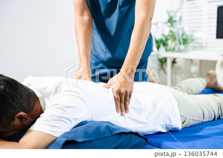 Male physiotherapist performs spine and arm adjustment therapy for patient on bed. Manual therapy, pain relief, posture alignment Male physiotherapist performs spine and arm adjustment therapy for patient on bed. Manual therapy, pain relief, posture alignment 136035744