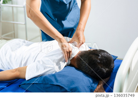 Male physiotherapist performs spine and arm adjustment therapy for patient on bed. Manual therapy, pain relief, posture alignment Male physiotherapist performs spine and arm adjustment therapy for patient on bed. Manual therapy, pain relief, posture alignment 136035749