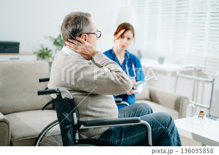 A caring nurse in blue scrubs conducts a neck pain consultation with a senior wheelchair patient at home A caring nurse in blue scrubs conducts a neck pain consultation with a senior wheelchair patient at home 136035858